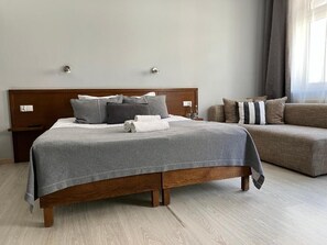 Ένα υπνοδωμάτιο με ένα ξύλινο κρεβάτι, γκρι κλινοσκεπάσματα, έναν καναπέ και ένα κομοδίνο.
