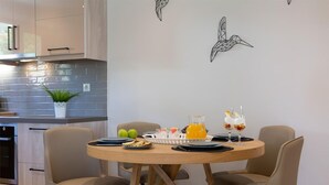 Une cuisine moderne avec un coin repas, comprenant une table ronde en bois entourée de quatre chaises, une plante en pot et une œuvre d’art représentant des oiseaux, accrochée au mur.