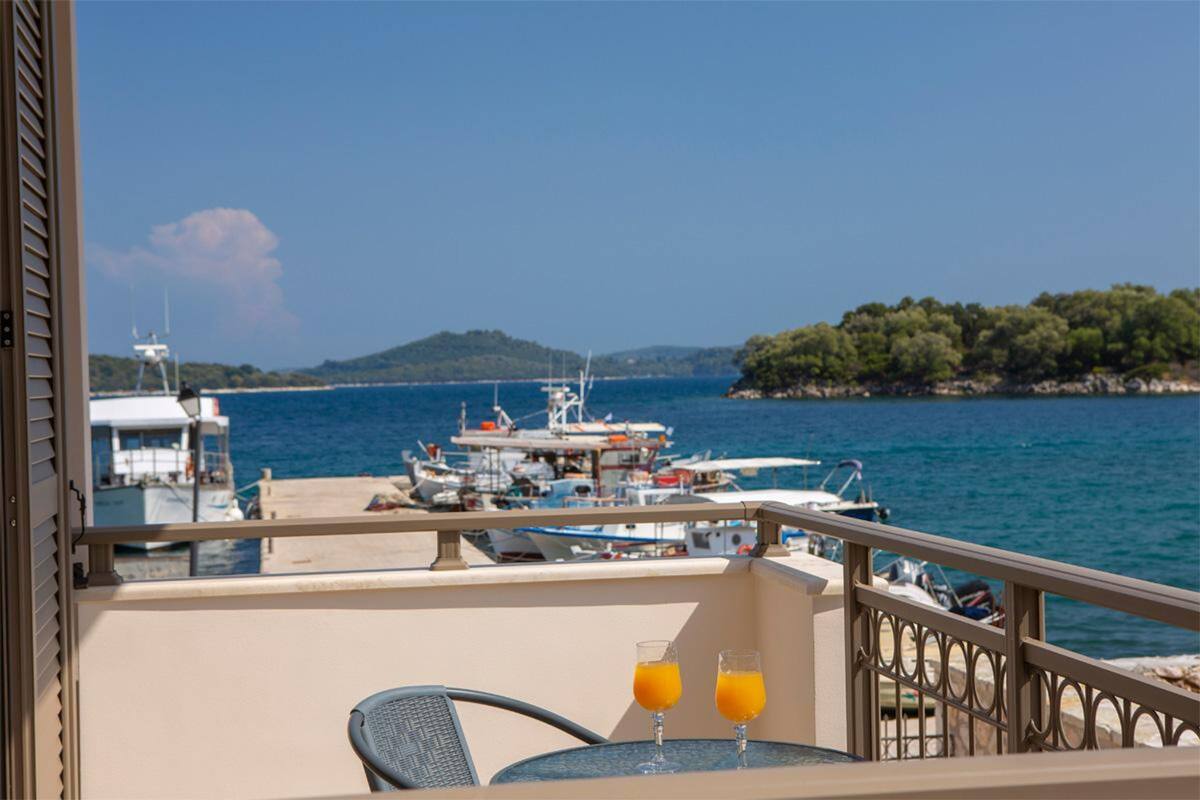 Ένα μπαλκόνι με ένα τραπέζι και δύο ποτήρια χυμό πορτοκαλιού, με θέα σε μια μαρίνα με σκάφη και ένα λόφωμα στο βάθος.
