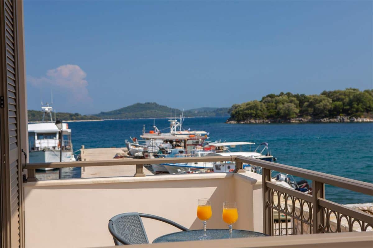A balcony with a table and two glasses of orange juice, overlooking a marina with boats and a hilly landscape.