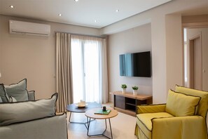 A modern living room with a sofa, a yellow armchair, a coffee table, a flat-screen TV, and a window with curtains. - Enalion Apartments (Lefkada)