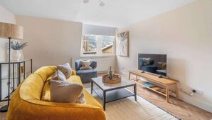 Un salon avec un canapé, un fauteuil, une table basse, un téléviseur et une fenêtre.