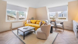 A modern living room with a sofa, armchair, coffee table, and dining table. - Boutique Bath Apartment, Close to Shops - VAT Q (Bath)