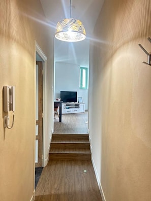 A hallway with a staircase leading to a living area, a telephone on the wall, and a patterned ceiling light. - 2 bedroom apartment - Downtown Parthenay (Parthenay)
