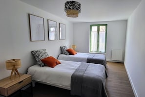 A bedroom with two beds, a window with green shutters, and a hanging light fixture. - 2 bedroom apartment - Downtown Parthenay (Parthenay)