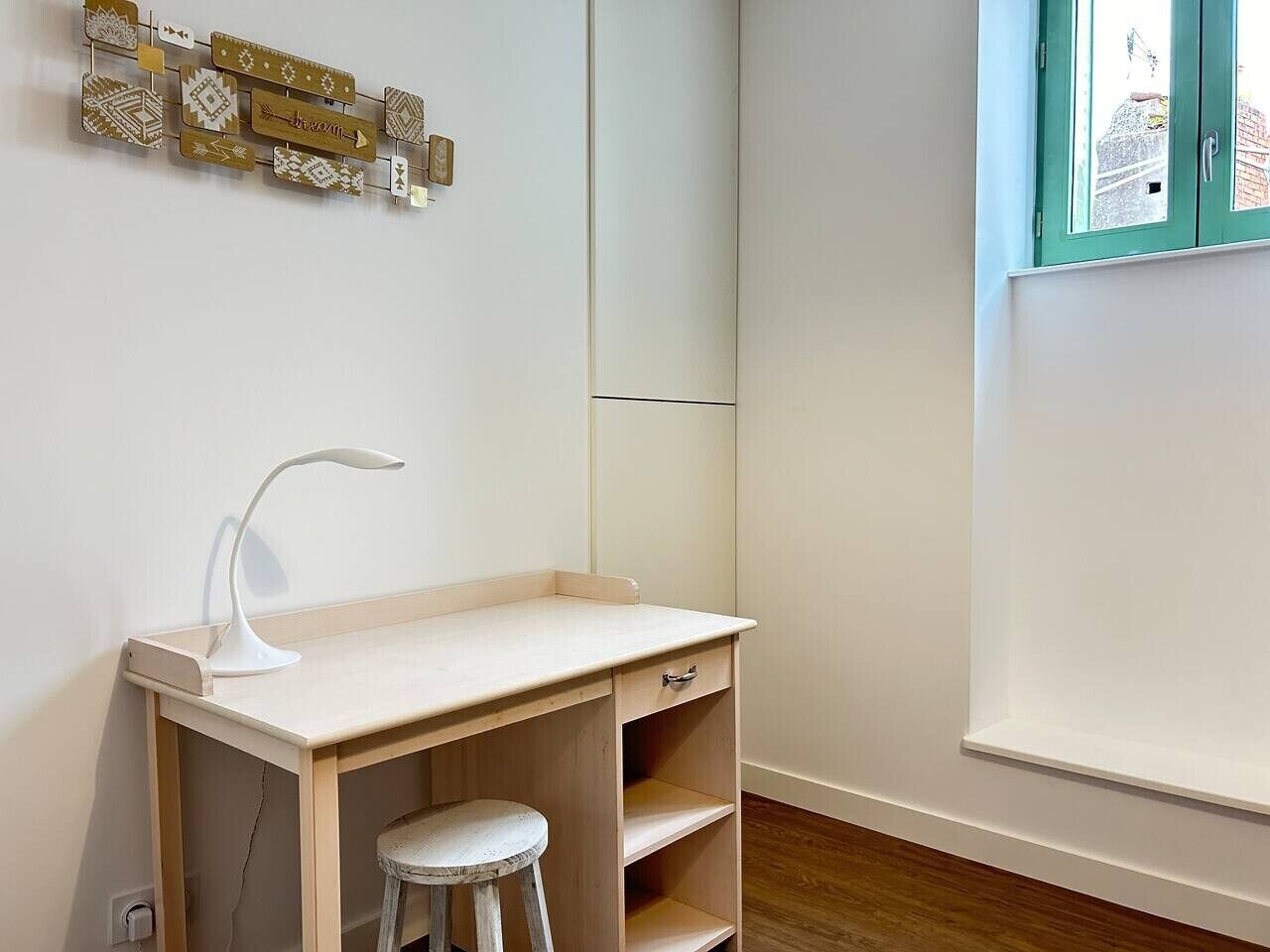 Een kinderbureau met een kruk, een witte bureaulamp en een wanddecoratie.