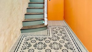 Una scala con ringhiera bianca, un pavimento decorato e una porta su un muro arancione.