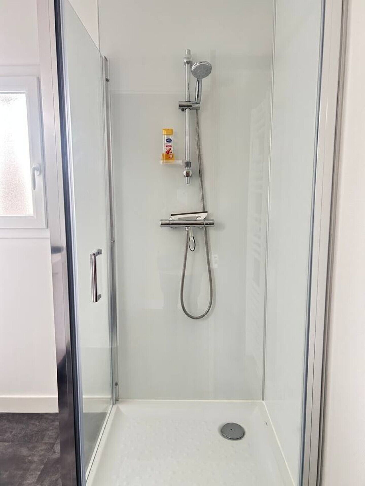 A glass-enclosed shower with a handheld showerhead and a wall-mounted faucet.