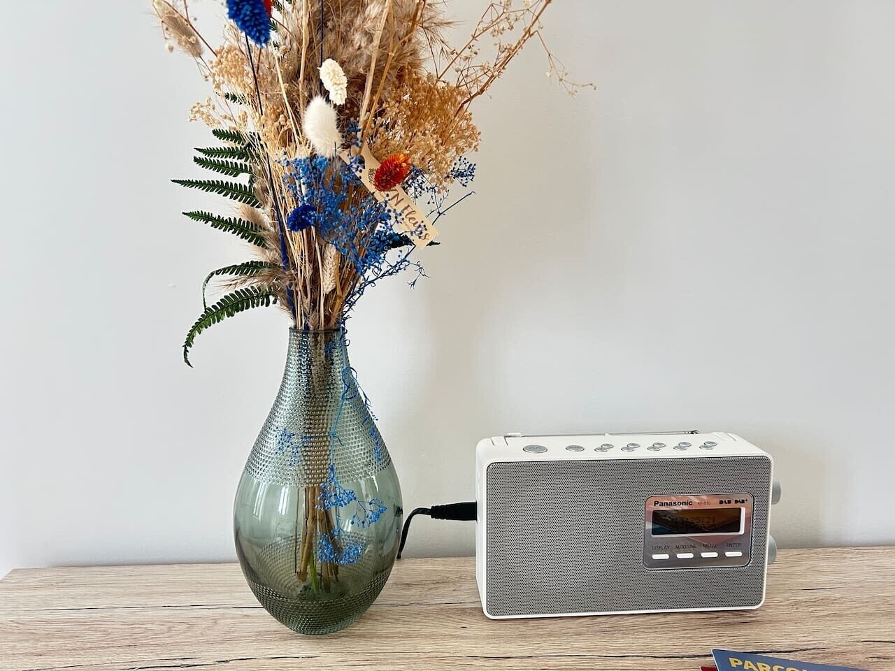 A vase with dried flowers and a vintage Panasonic radio on a wooden surface.