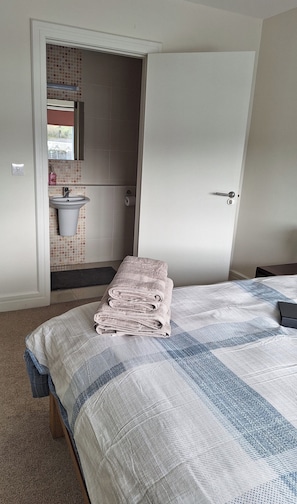 Un dormitorio con cama, un baño con lavamanos y espejo, y una puerta que da a otra habitación.