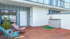 A modern outdoor area with a wooden deck, a seating area with a chair and a small table, and a potted plant. - Centrally Located 2bed Duplex (Westport)