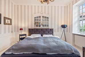 Ein Schlafzimmer mit einem gesteppten Kopfteil, einem großen Bett, einem Nachttisch mit Lampe, einer Stehlampe und einem Fenster mit Blick.