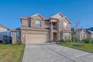 A two-story house with a stone facade, a garage, and a front yard. - Spacious 6-bedroom house with lake in beautiful Missouri City (Missouri City)
