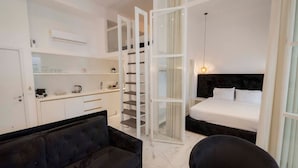 A hotel room with a bed, a sofa, a desk, and a staircase leading to an upper level. - 4 Elemental Living Suites - Wind (Nea Moudania)