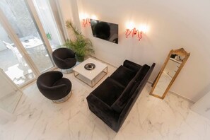 A modern living room with a sofa, two armchairs, a coffee table, a flat-screen TV, a wall-mounted light fixture, and a large mirror. - 4 Elemental Living Suites - Wind (Nea Moudania)