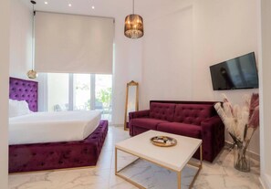 A modern hotel room with a bed, a sofa, a coffee table, a TV, and a large window. - 4 Elemental Living Suites - Earth (Nea Moudania)