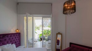Een slaapkamer met een bed, een spiegel, een rode bank en een schuifglazen deur die leidt naar een buitenruimte.