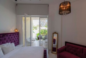 A bedroom with a bed, a mirror, a red sofa, and a sliding glass door leading to an outdoor area. - 4 Elemental Living Suites - Earth (Nea Moudania)