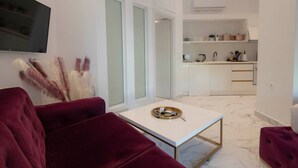 Een moderne woonkamer met een rode bank, een witte salontafel en een keuken op de achtergrond.