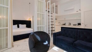 Ein modernes Hotelzimmer mit einem Bett, einer dunkelblauen Couch, einem schwarzen Sessel und einem weißen Kleiderschrank.