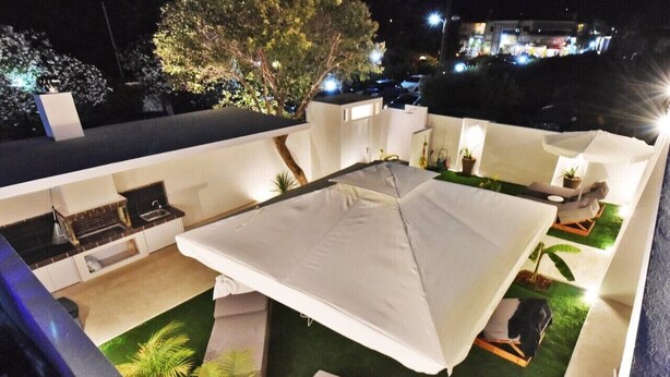 Une terrasse sur le toit avec un espace salon couvert, une petite cuisine et des plantes en pot.