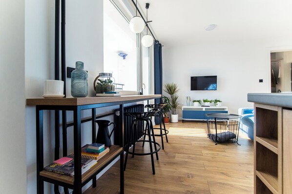 A modern kitchen with a wooden countertop, black bar stools, a round table, and a TV mounted on the wall.
