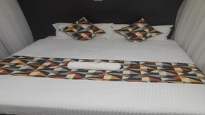 A neatly made bed with a patterned bedspread and pillows, a white headboard, and a dark floor. - Ohm Village Inn (Kitui)