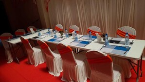 A conference room with tables set for meetings, chairs with orange sashes, and a red carpeted floor. - Ohm Village Inn (Kitui)