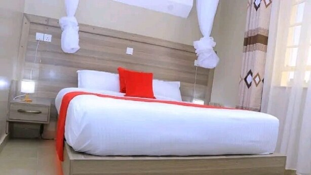 A single bed with a wooden headboard, a bedside table, and a red pillow. - Ohm Village Inn (Kitui)