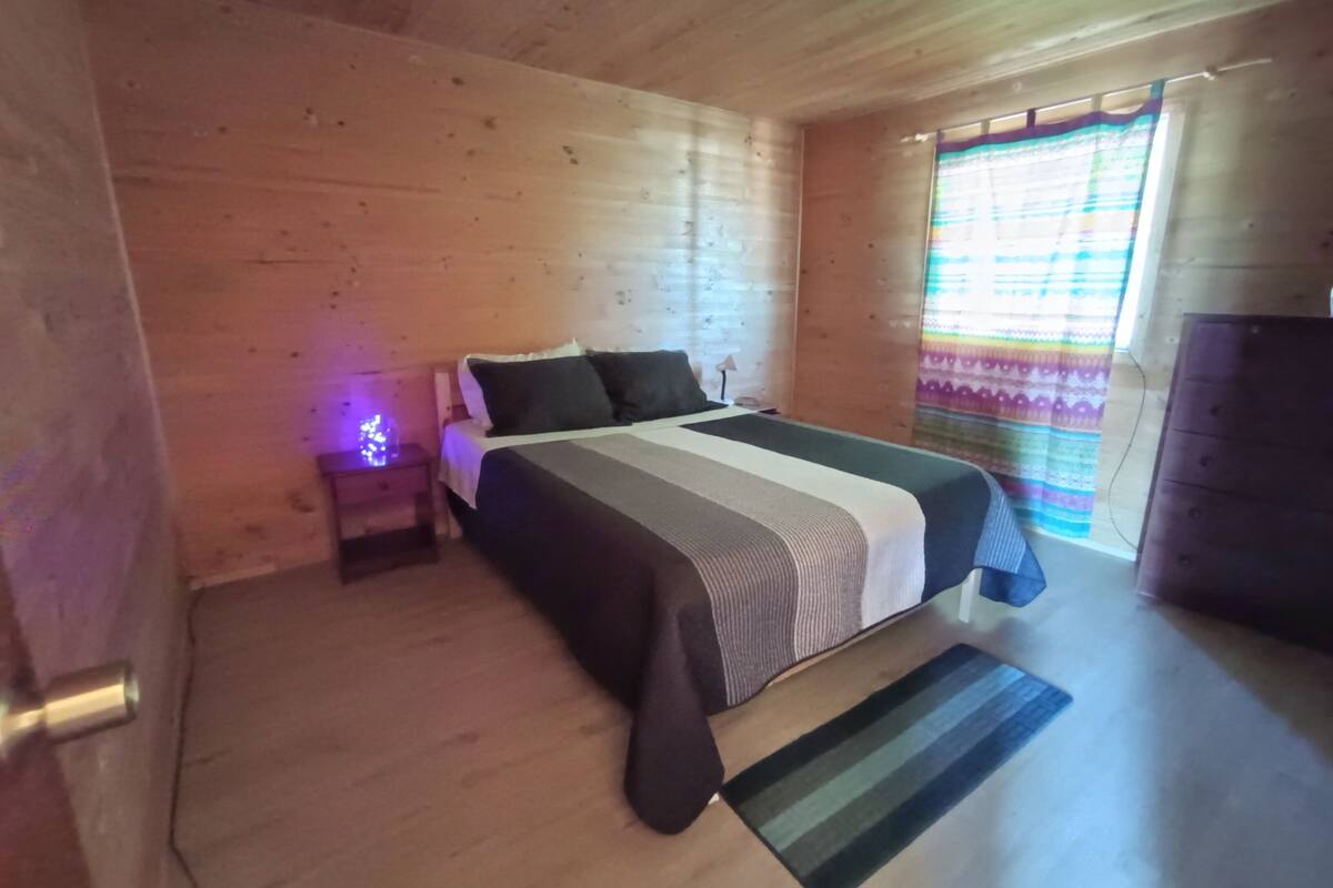Une chambre dans une cabane en bois, avec un lit, une table de chevet et une commode.