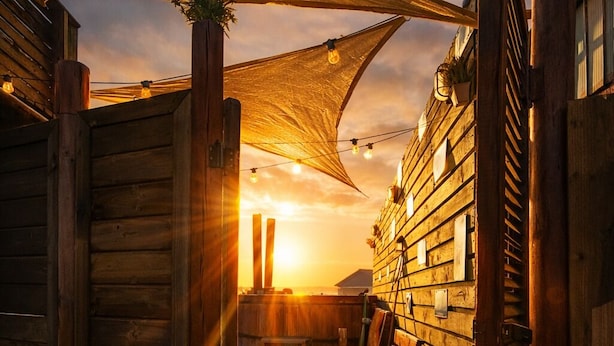 A wooden deck with a bench and a table, a wooden fence, and a building with windows. - Haré Tauromi (El Tabo)