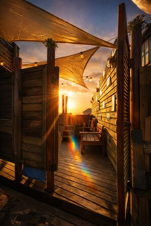 A wooden deck with a bench and a table, a wooden fence, and a building with windows. - Haré Tauromi  (El Tabo)