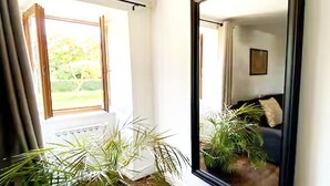 Ein Zimmer mit einem großen Spiegel, einem fenster mit Vorhängen und Topfpflanzen.
