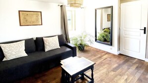 Ein Wohnzimmer mit einer schwarzen Couch, einem kleinen Holztisch, einem großen Spiegel und einer Tür.