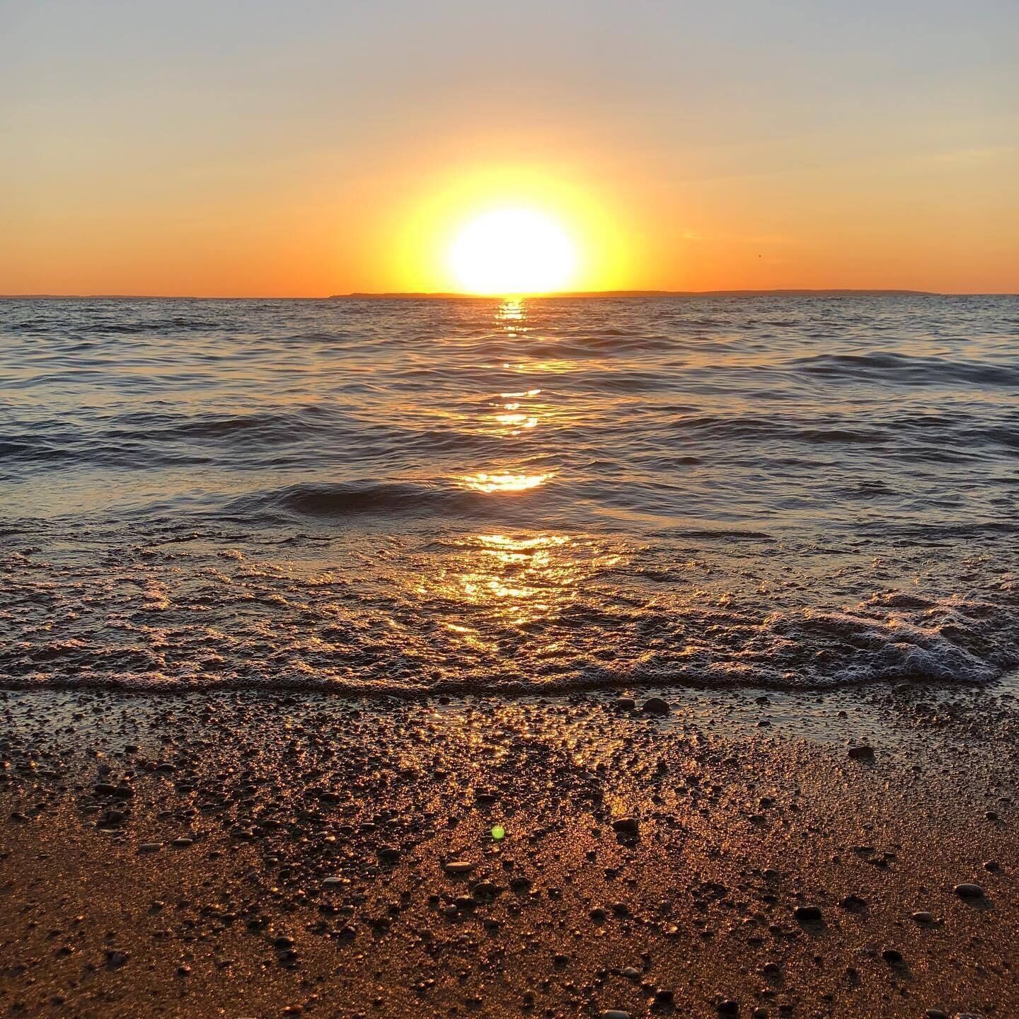 A sunset over a beach with waves and pebbles.