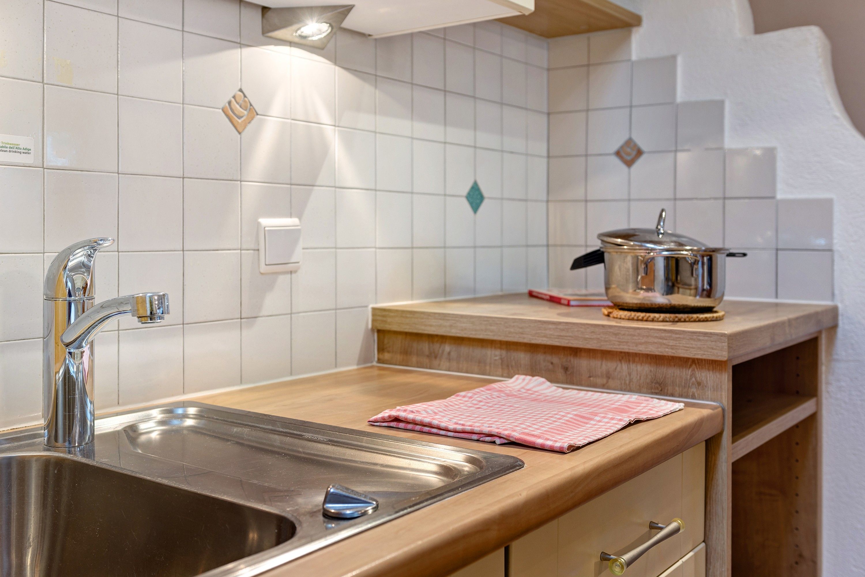 A kitchen with a stainless steel sink, a wooden countertop, a pot on the stove, and a tiled backsplash.