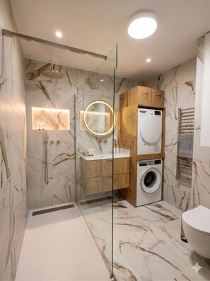 A modern bathroom with a glass-enclosed shower, marble walls, a wooden vanity, and a built-in washing machine. - 3-Bedroom Apartment with Terrace • Air Conditioning • Parking • Near the Beaches • Ideal for Families (Fréjus)