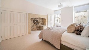 A bedroom with a stone fireplace, a bed with pillows, a white wardrobe, and a window with a view.