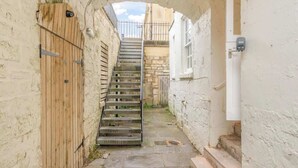 A narrow alleyway with a wooden door and a metal staircase leading to a higher level.