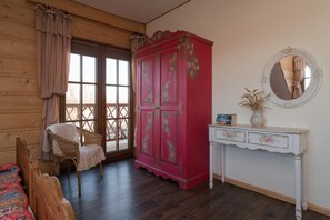 A room with a wooden floor, a wicker chair, a red cabinet with floral designs, a white console table with drawers, and a round mirror on the wall. - Comfortable apartment, 2 levels, close to beach (Ustronie Morskie)