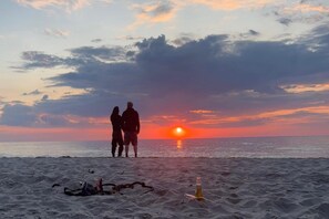 A beach scene with two silhouettes of people standing facing the sunset. - Comfortable apartment, 2 levels, close to beach (Ustronie Morskie)