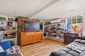A living room with a wooden cabinet, a television, a bookshelf, and a large window. - The Birdcage - Walk to CBD - Free Parking (West Hobart)