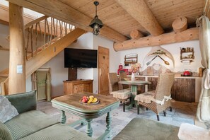 Ein rustikales Interieur mit einer Holztreppe, einem Essbereich mit Tisch und Stühlen, einem Fernseher und einer Küchenzeile mit einem roten Gerät.