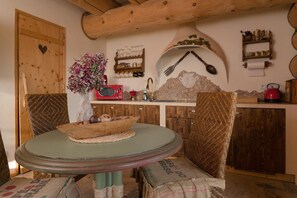 A rustic kitchen with wooden cabinets, a round table, wicker chairs, a vase with flowers, and a red kettle. - Comfortable apartment very close to the beach (Ustronie Morskie)