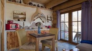 Un intérieur rustique en bois, avec une table à manger, des chaises en osier, un vase rempli de fleurs et une grande fenêtre agrémentée de rideaux.
