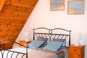 Ein Schlafzimmer mit schrägen Wänden, einem Metallbettgestell, zwei Nachttischen mit Lampen und zwei an der Wand befestigten Bildern.