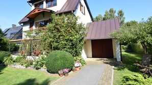 Ein zweigeschossiges Haus mit einem geneigten Dach, einer Garage und einem gepflegten Garten mit verschiedenen Pflanzen und Blumen.