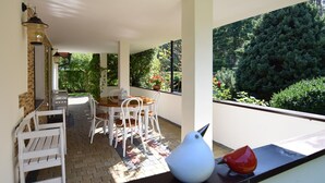 Ein überdachter Patio-Bereich mit Tisch und Stühlen, einer weißen Vogel-Skulptur und Blick ins Grüne.