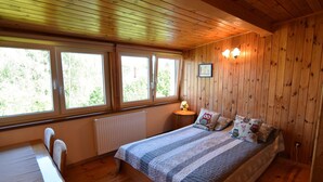 Ein Schlafzimmer mit Holzwänden, einem Bett, zwei Fenstern, einem Tisch und einem Stuhl.