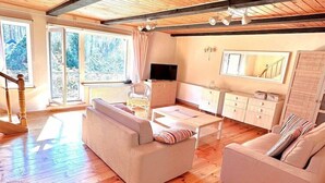 Ein modernes Wohnzimmer mit einer Couch, einem Couchtisch und einem Fernseher. Eine Treppe führt zu einer oberen Ebene.
